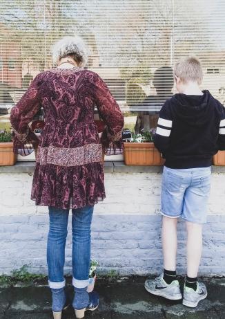 Een oma en haar kleinzoon vullen samen bloembakken met bloemen. 