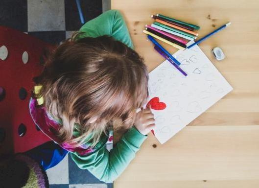 Een kindje tekent verschillende hartjes en kleurt een hartje rood in. 