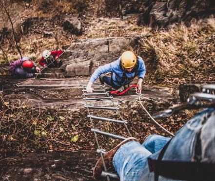 Een groep mensen klimmen met een ladder een berg omhoog. 